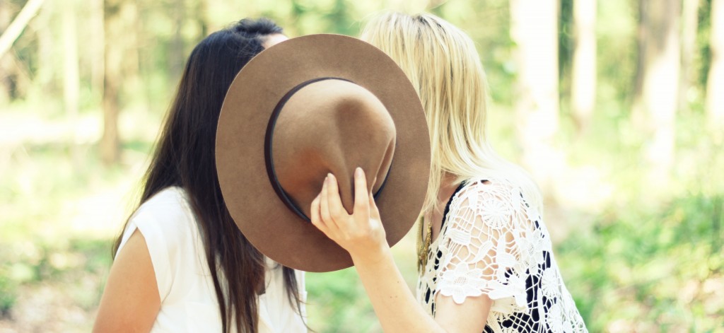 twee vrouwen zoenen achter hoed